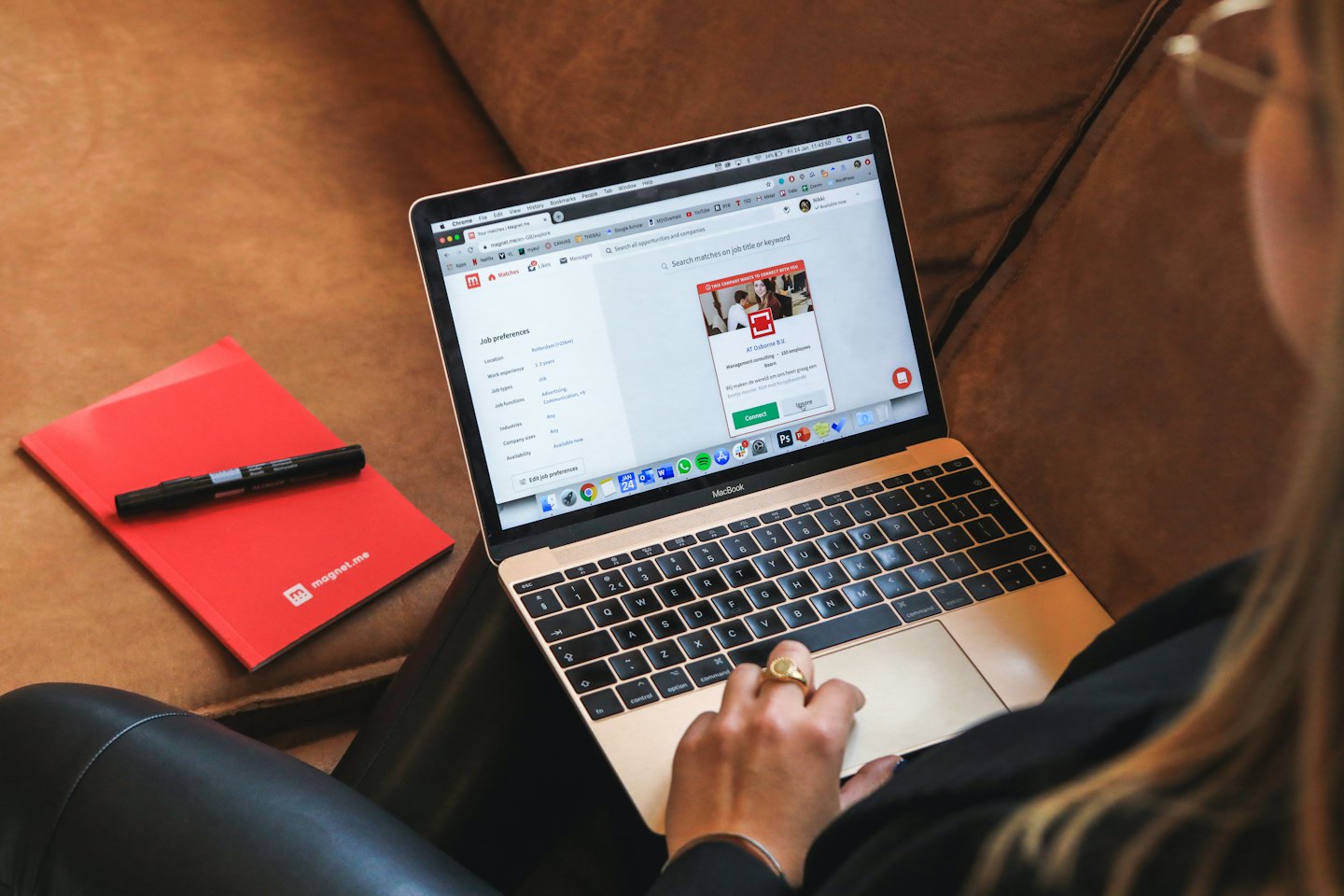 茶色のソファで、金色のMacBookを使って求人を探している人。
